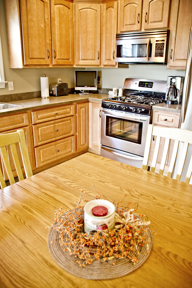 Inredning av ett klassiskt mellanstort kök, med en nedsänkt diskho, luckor med upphöjd panel, skåp i ljust trä, laminatbänkskiva, svarta vitvaror, klinkergolv i keramik och en köksö