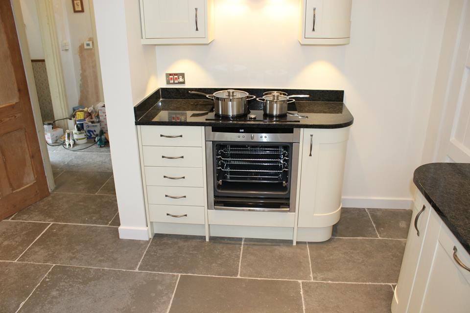 Photo of a large country kitchen/diner in Dorset with a built-in sink, shaker cabinets, beige cabinets, granite worktops, black splashback, coloured appliances, limestone flooring and an island.