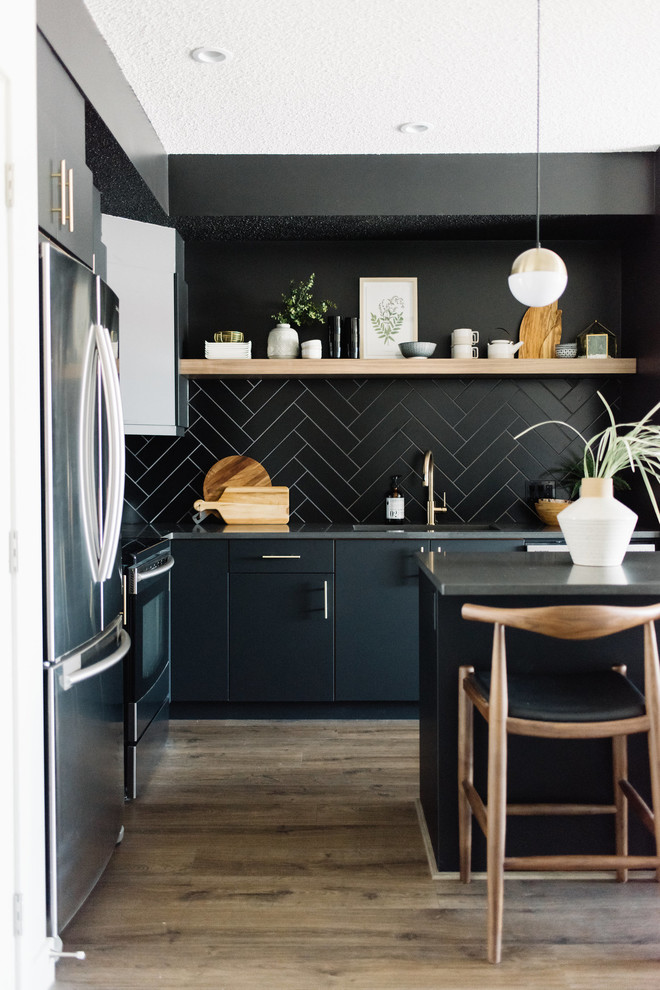 Skandinavische Küche in L-Form mit flächenbündigen Schrankfronten, schwarzen Schränken, Küchenrückwand in Schwarz, Küchengeräten aus Edelstahl, braunem Holzboden, Kücheninsel und grauer Arbeitsplatte in Edmonton