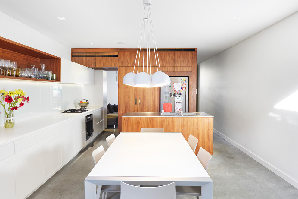 Design ideas for a small contemporary kitchen/diner in Sydney with an integrated sink, flat-panel cabinets, white splashback, glass sheet splashback, stainless steel appliances, concrete flooring, an island and medium wood cabinets.