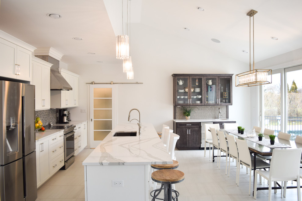 Example of a mid-sized transitional single-wall marble floor eat-in kitchen design in New York with an undermount sink, shaker cabinets, white cabinets, quartz countertops, gray backsplash, glass tile backsplash, stainless steel appliances and an island
