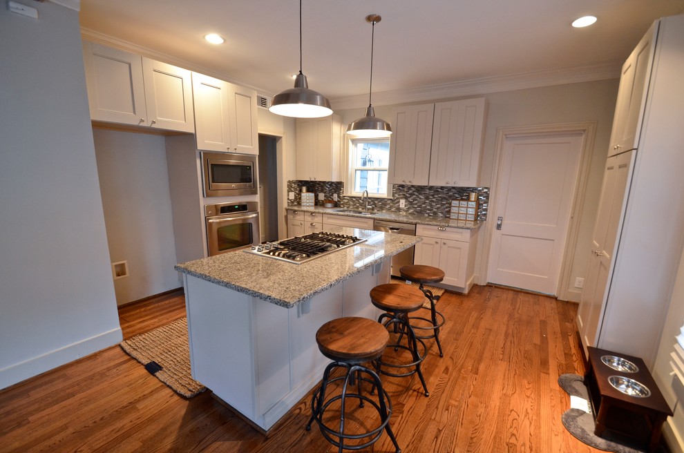 Bild på ett eklektiskt kök, med en undermonterad diskho, skåp i shakerstil, grå skåp, granitbänkskiva, stänkskydd med metallisk yta, glaspanel som stänkskydd, rostfria vitvaror, mellanmörkt trägolv och en köksö