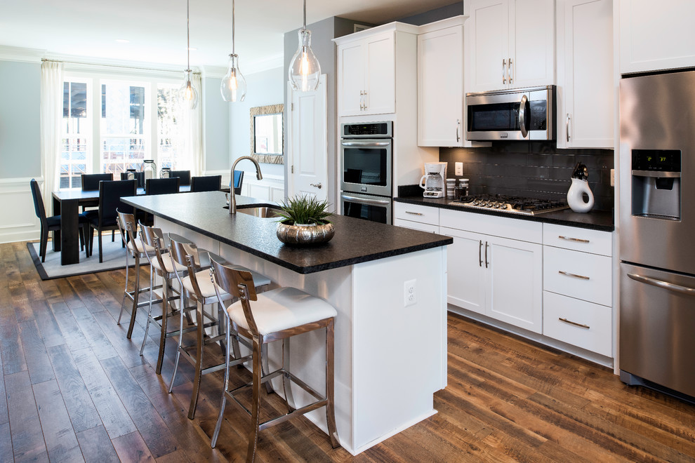 Photo of a transitional eat-in kitchen in DC Metro with an undermount sink, shaker cabinets, white cabinets, black splashback, stainless steel appliances, dark hardwood floors, with island and brown floor.