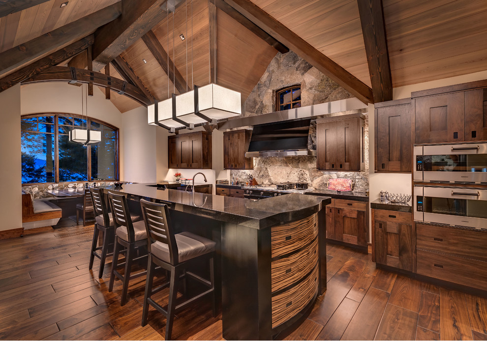Cette photo montre une grande cuisine montagne en bois foncé avec un placard avec porte à panneau encastré, un sol en bois brun, îlot et un électroménager en acier inoxydable.