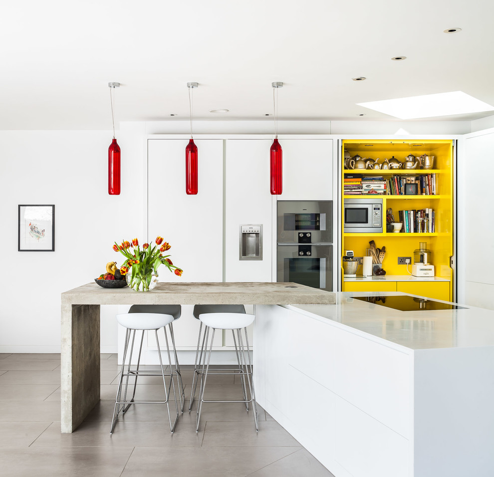 Moderne Küche mit flächenbündigen Schrankfronten, weißen Schränken, Küchengeräten aus Edelstahl und Kücheninsel in London