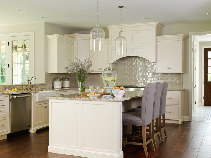 Inspiration for a large cottage l-shaped medium tone wood floor eat-in kitchen remodel in Minneapolis with a farmhouse sink, recessed-panel cabinets, white cabinets, granite countertops, beige backsplash, ceramic backsplash, stainless steel appliances and an island
