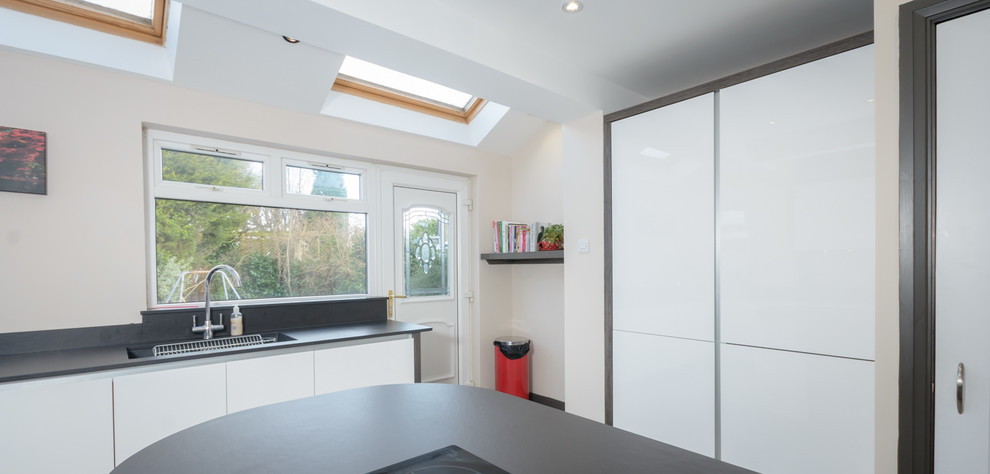 Cette image montre une petite cuisine design avec des portes de placard blanches et un électroménager en acier inoxydable.