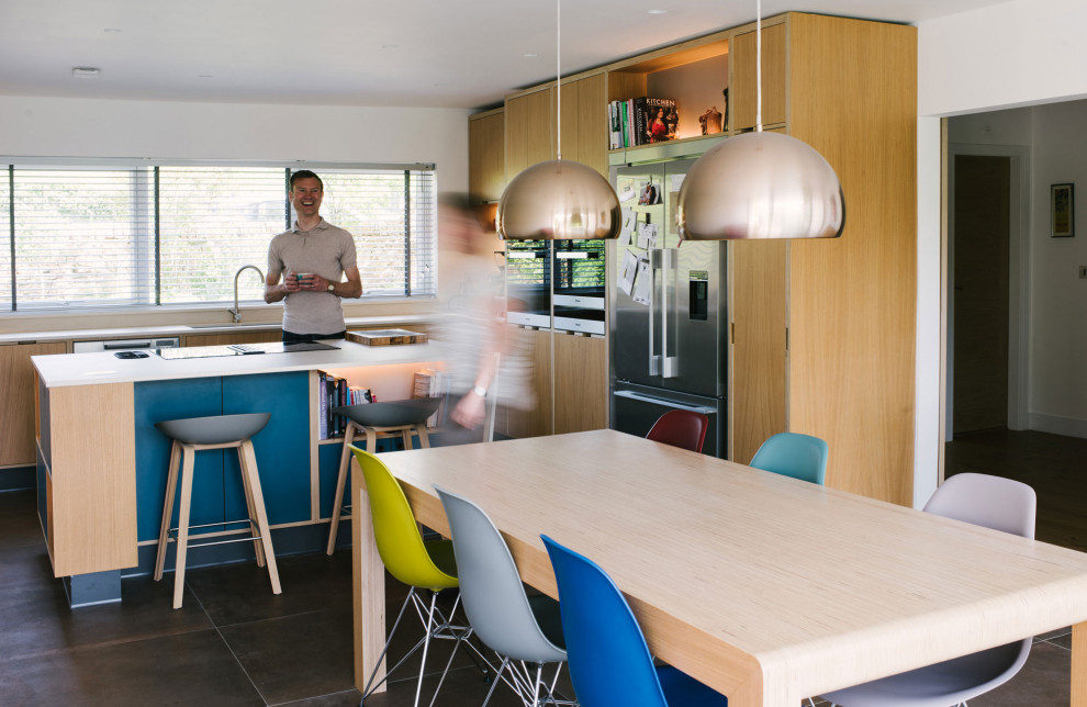 This is an example of a scandi l-shaped kitchen/diner in Other with a submerged sink, flat-panel cabinets, light wood cabinets, stainless steel appliances, an island, brown floors and white worktops.