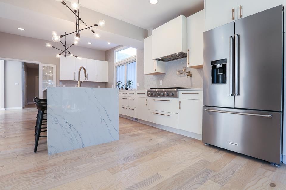 Example of a large trendy l-shaped light wood floor and beige floor enclosed kitchen design in Baltimore with an undermount sink, flat-panel cabinets, white cabinets, marble countertops, gray backsplash, ceramic backsplash, stainless steel appliances, an island and white countertops