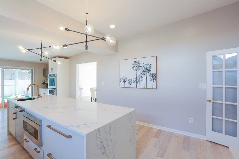 Large trendy l-shaped light wood floor and beige floor enclosed kitchen photo in Baltimore with an undermount sink, flat-panel cabinets, white cabinets, marble countertops, gray backsplash, ceramic backsplash, stainless steel appliances, an island and white countertops
