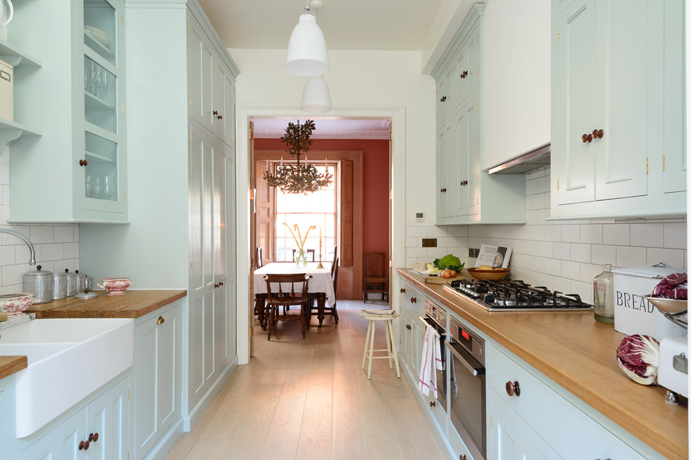 Medium sized traditional galley enclosed kitchen in London with a double-bowl sink, beaded cabinets, blue cabinets, wood worktops, white splashback, metro tiled splashback, stainless steel appliances, light hardwood flooring and no island.