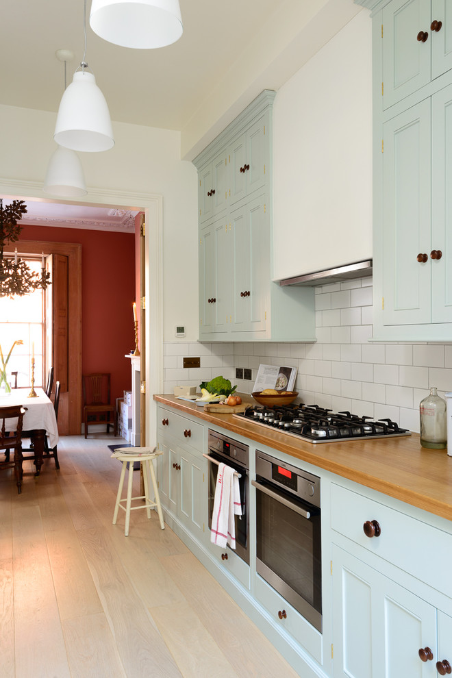 Design ideas for a medium sized traditional single-wall enclosed kitchen in London with beaded cabinets, blue cabinets, wood worktops, white splashback, metro tiled splashback, stainless steel appliances, light hardwood flooring and no island.