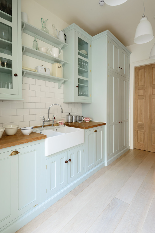Photo of a medium sized classic galley enclosed kitchen in London with a double-bowl sink, beaded cabinets, blue cabinets, wood worktops, white splashback, metro tiled splashback, stainless steel appliances, light hardwood flooring and no island.