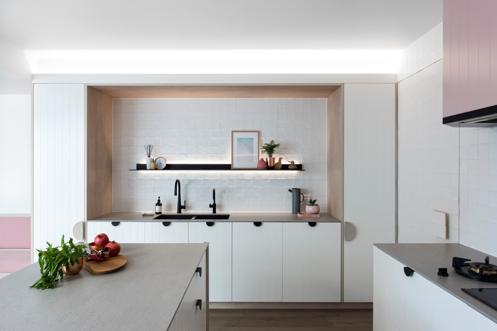 Inspiration for a medium sized contemporary l-shaped open plan kitchen in Sydney with a double-bowl sink, white cabinets, recycled glass countertops, white splashback, cement tile splashback, black appliances, medium hardwood flooring, an island and grey worktops.