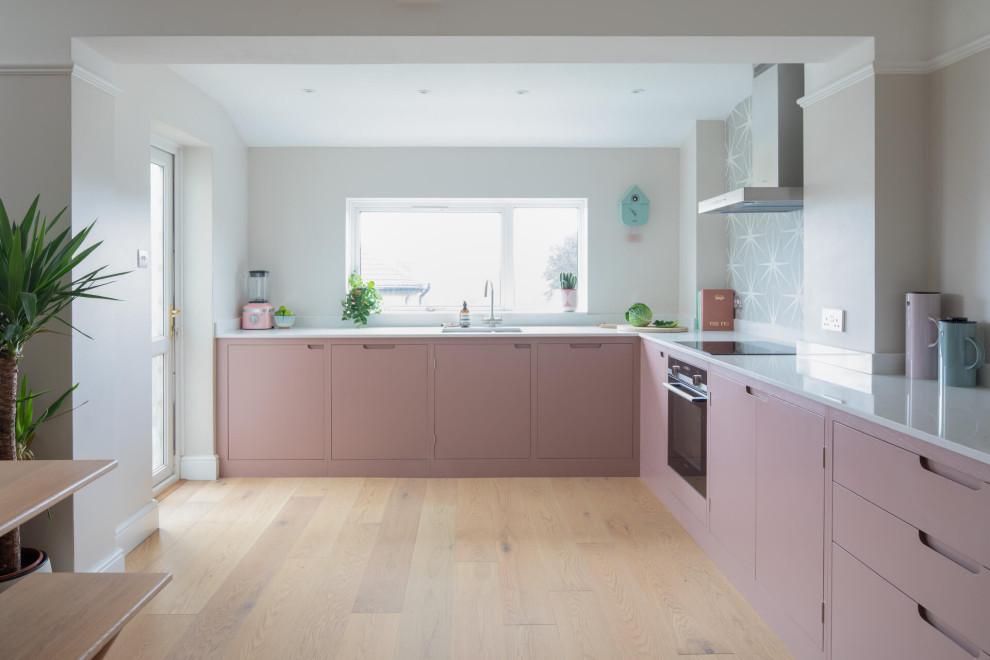 Diseño de cocina nórdica de tamaño medio sin isla con armarios con paneles lisos, puertas de armarios rosa, encimera de cuarzo compacto, suelo de madera clara y encimeras blancas