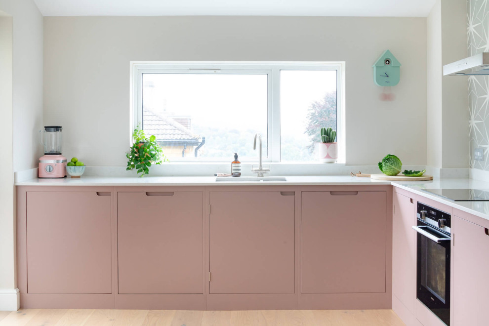 Foto de cocina nórdica de tamaño medio sin isla con armarios con paneles lisos, puertas de armarios rosa, encimera de cuarzo compacto, suelo de madera clara y encimeras blancas