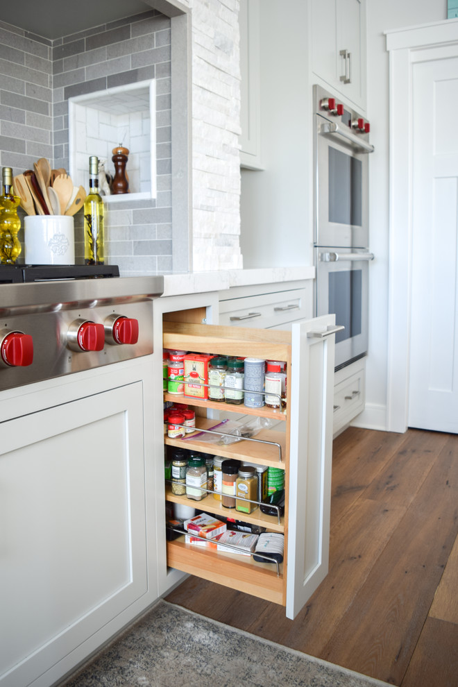 Example of a mid-sized beach style u-shaped medium tone wood floor eat-in kitchen design in New York with an undermount sink, shaker cabinets, gray cabinets, quartz countertops, gray backsplash, slate backsplash, paneled appliances and an island