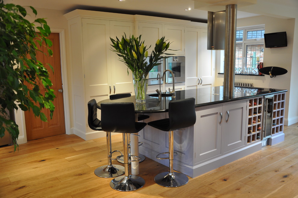 Example of a mid-sized transitional u-shaped medium tone wood floor eat-in kitchen design in Hertfordshire with a drop-in sink, recessed-panel cabinets, beige cabinets, granite countertops, stainless steel appliances and an island