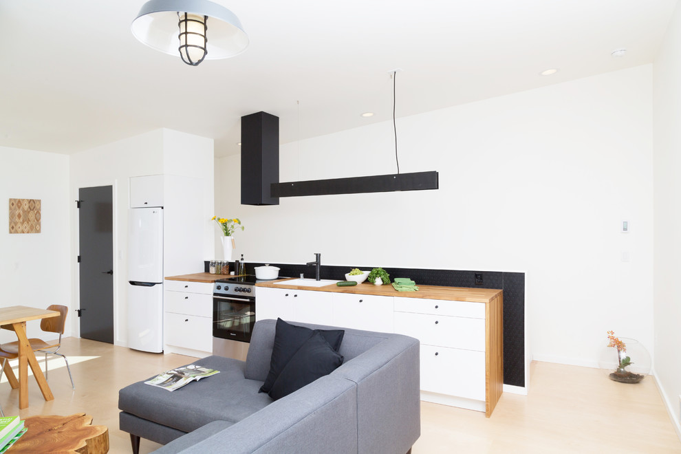 Inspiration for a small contemporary single-wall open plan kitchen in Seattle with a single-bowl sink, flat-panel cabinets, white cabinets, wood worktops, black splashback, white appliances, plywood flooring, no island, white floors and brown worktops.