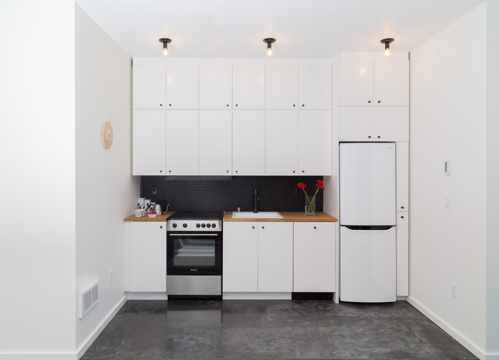 Modern inredning av ett litet brun linjärt brunt kök med öppen planlösning, med en enkel diskho, släta luckor, vita skåp, träbänkskiva, svart stänkskydd, vita vitvaror, plywoodgolv och vitt golv
