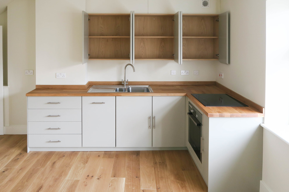 Exempel på ett litet modernt l-kök, med en dubbel diskho, släta luckor, grå skåp, träbänkskiva, rostfria vitvaror och mellanmörkt trägolv