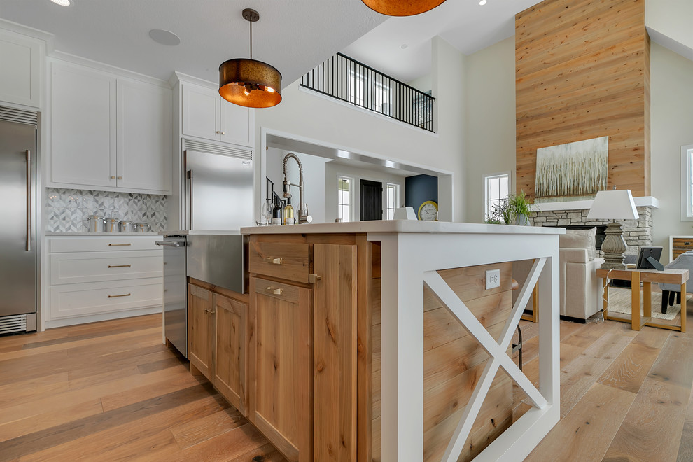 Small farmhouse l-shaped open plan kitchen in Minneapolis with a belfast sink, shaker cabinets, white cabinets, quartz worktops, grey splashback, stainless steel appliances, medium hardwood flooring, an island, brown floors and white worktops.