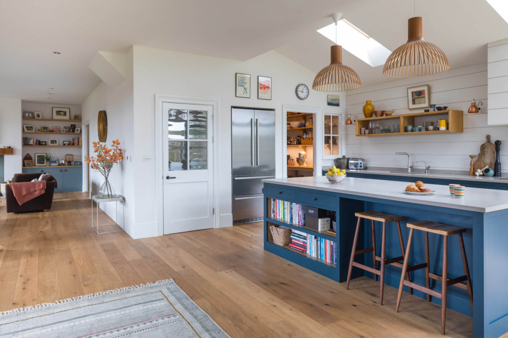 Medium sized contemporary open plan kitchen in Other with a built-in sink, shaker cabinets, blue cabinets, quartz worktops, light hardwood flooring, an island and white worktops.