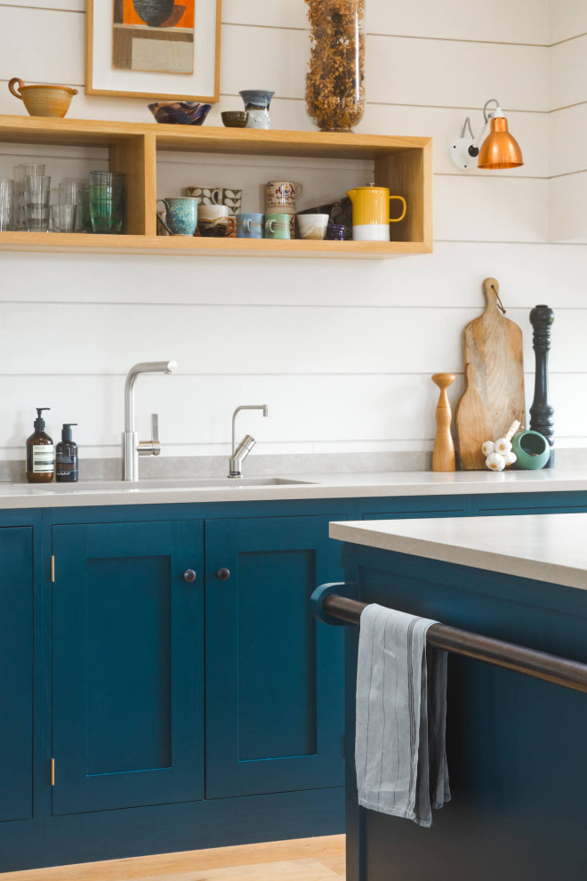 Inredning av ett modernt mellanstort vit vitt kök med öppen planlösning, med en nedsänkt diskho, skåp i shakerstil, blå skåp, bänkskiva i kvartsit, ljust trägolv och en köksö