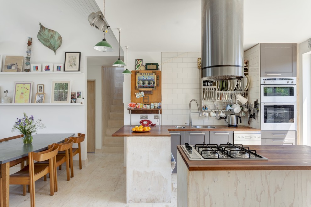 Foto på ett maritimt brun kök, med en nedsänkt diskho, skåp i shakerstil, grå skåp, träbänkskiva, vitt stänkskydd, stänkskydd i tunnelbanekakel, rostfria vitvaror, plywoodgolv, en köksö och beiget golv