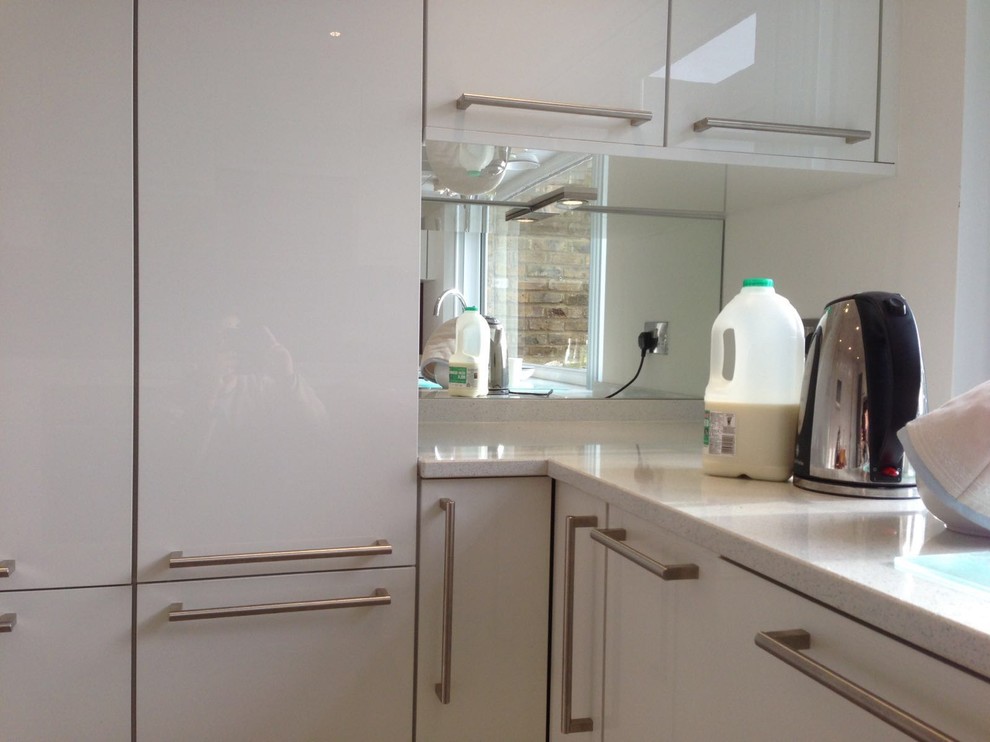 Foto på ett avskilt, litet funkis u-kök, med en integrerad diskho, släta luckor, vita skåp, rött stänkskydd, glaspanel som stänkskydd och rostfria vitvaror