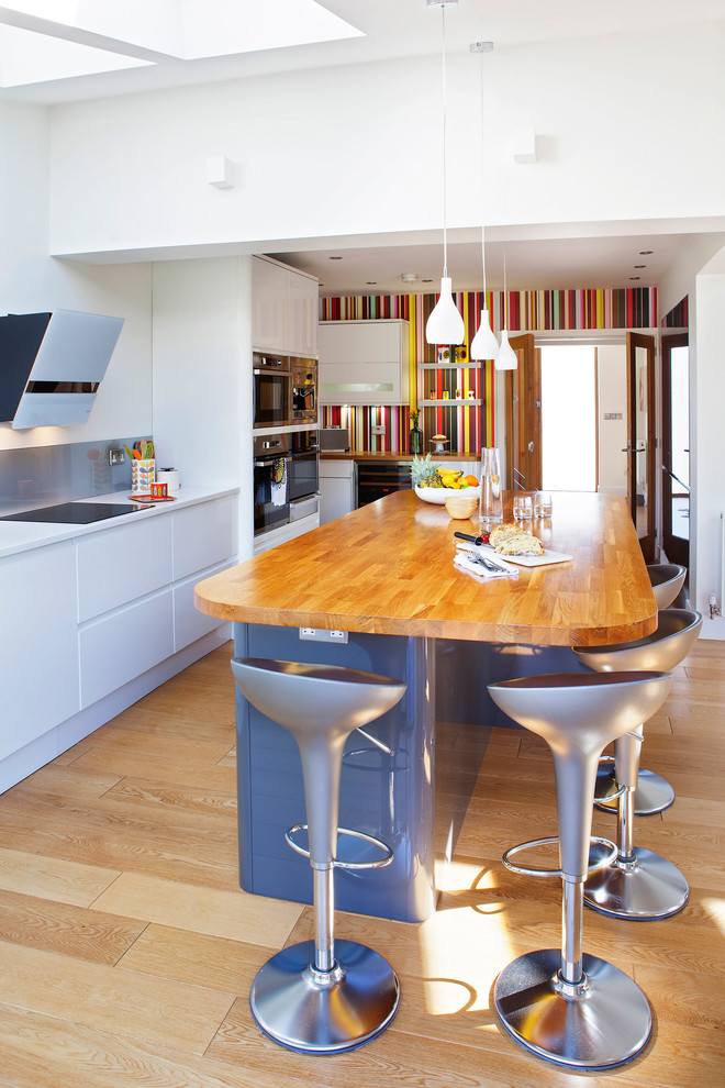Große Moderne Küche in L-Form mit flächenbündigen Schrankfronten, weißen Schränken, Arbeitsplatte aus Holz, hellem Holzboden und Kücheninsel in Sonstige