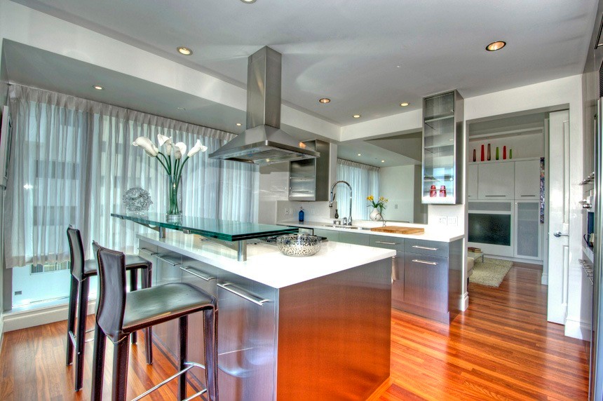 Bild på ett mellanstort funkis kök, med släta luckor, skåp i rostfritt stål, rostfria vitvaror, mellanmörkt trägolv och en köksö