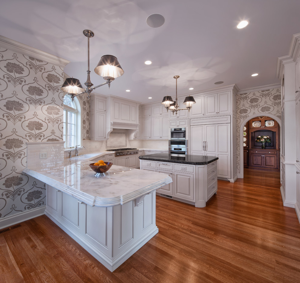 Exempel på ett stort klassiskt kök, med en undermonterad diskho, luckor med upphöjd panel, vita skåp, marmorbänkskiva, vitt stänkskydd, stänkskydd i tunnelbanekakel, integrerade vitvaror, mellanmörkt trägolv och en köksö