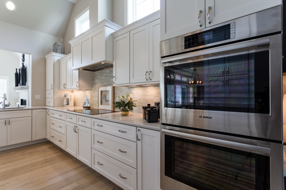 Klassisk inredning av ett u-kök, med en undermonterad diskho, luckor med infälld panel, vita skåp, bänkskiva i kvarts, beige stänkskydd, rostfria vitvaror, ljust trägolv och en köksö