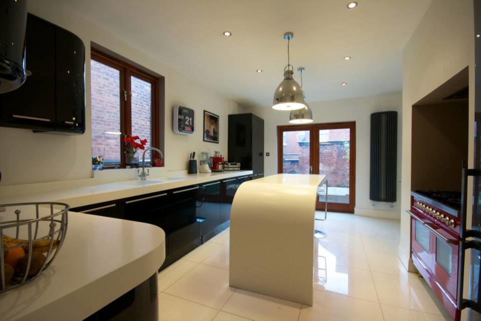 Große Moderne Wohnküche in L-Form mit integriertem Waschbecken, flächenbündigen Schrankfronten, schwarzen Schränken, Mineralwerkstoff-Arbeitsplatte, Küchenrückwand in Weiß, bunten Elektrogeräten, Keramikboden und Kücheninsel in Manchester