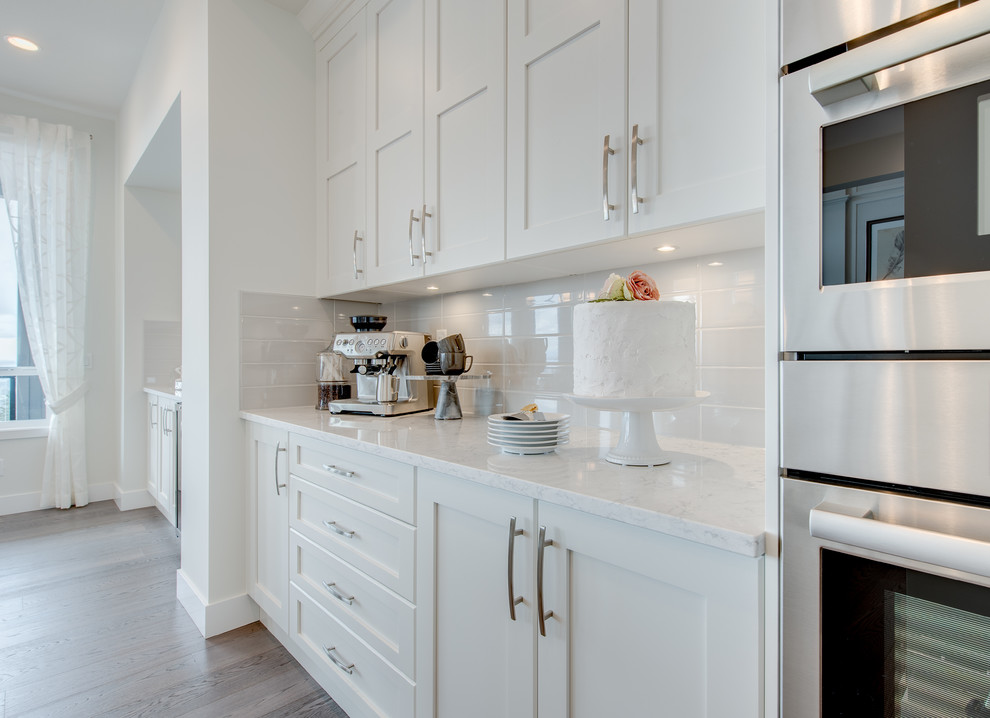 Moderne Küche mit Schrankfronten im Shaker-Stil, weißen Schränken, Küchenrückwand in Weiß, Rückwand aus Metrofliesen, Küchengeräten aus Edelstahl und Kücheninsel in Vancouver
