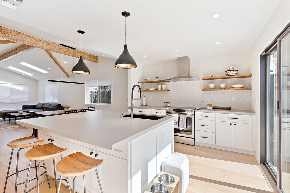 Inredning av ett modernt mellanstort grå linjärt grått kök med öppen planlösning, med en undermonterad diskho, skåp i shakerstil, vita skåp, vitt stänkskydd, rostfria vitvaror, ljust trägolv, en köksö och beiget golv