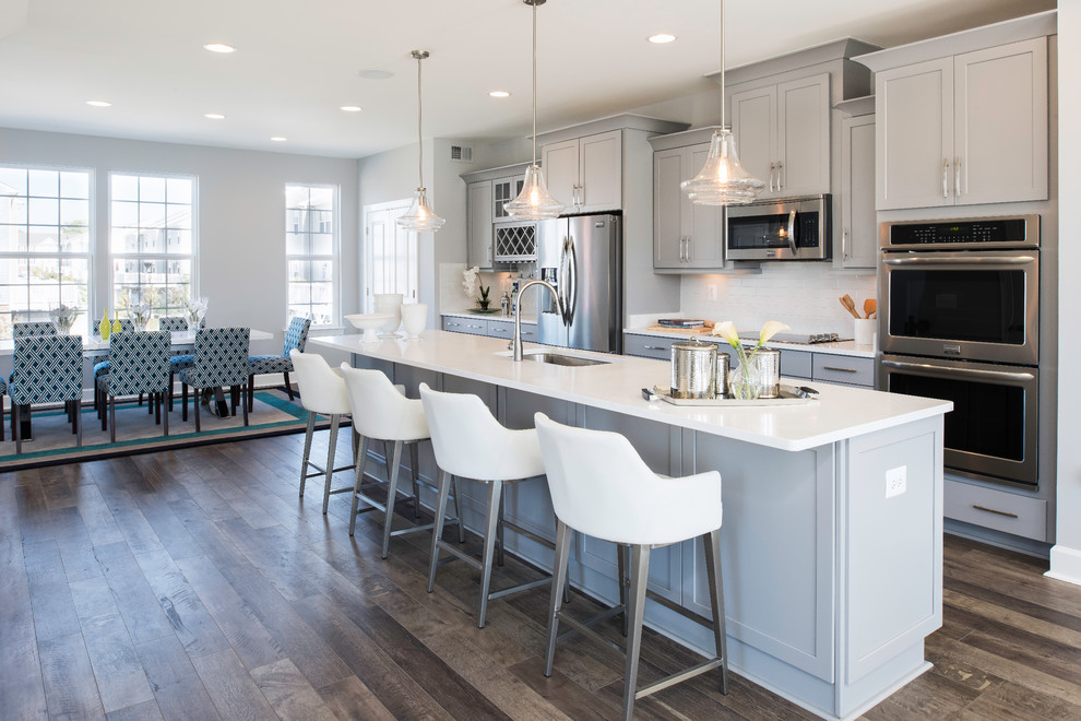 Foto de cocina comedor gris y blanca clásica renovada con fregadero bajoencimera, armarios estilo shaker, puertas de armario grises, salpicadero blanco, salpicadero de azulejos tipo metro, electrodomésticos de acero inoxidable, suelo de madera oscura y una isla