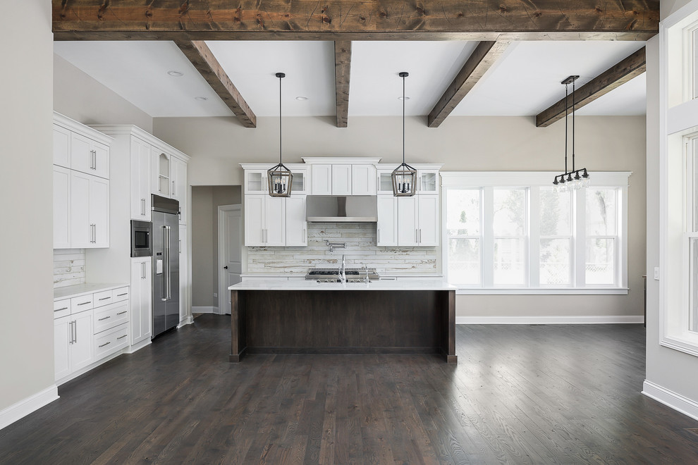 Expansive farmhouse l-shaped kitchen/diner in Chicago with a belfast sink, shaker cabinets, white cabinets, engineered stone countertops, white splashback, ceramic splashback, stainless steel appliances, dark hardwood flooring, an island, brown floors and white worktops.