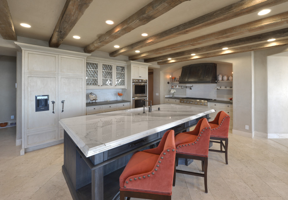 Example of a large tuscan u-shaped travertine floor and beige floor open concept kitchen design in San Francisco with an undermount sink, recessed-panel cabinets, white cabinets, white backsplash, subway tile backsplash, paneled appliances, an island, marble countertops and white countertops