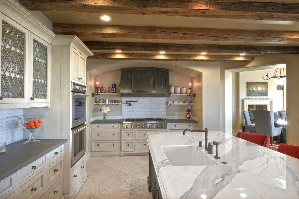 Inspiration for a mediterranean u-shaped travertine floor open concept kitchen remodel in San Francisco with an undermount sink, recessed-panel cabinets, white cabinets, marble countertops, white backsplash, subway tile backsplash, paneled appliances and an island