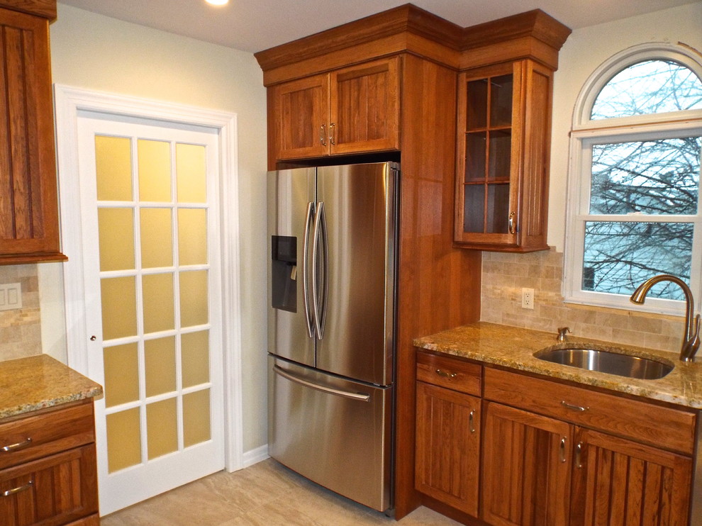 Example of a country galley limestone floor eat-in kitchen design in New York with a drop-in sink, raised-panel cabinets, light wood cabinets, granite countertops, beige backsplash, stone tile backsplash, stainless steel appliances and a peninsula