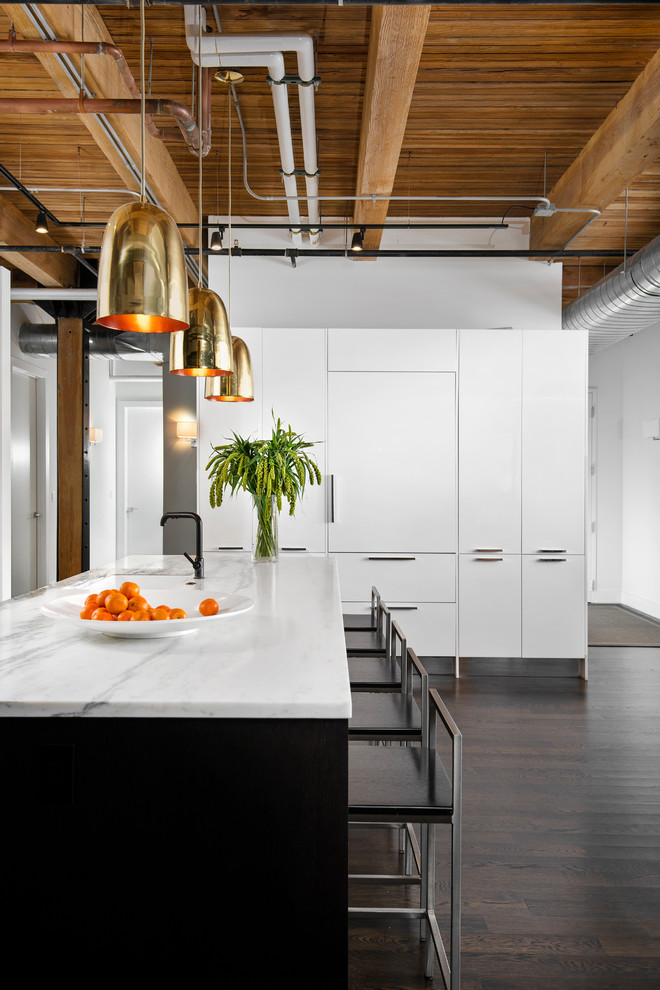 Photo of an industrial kitchen in Chicago with white cabinets, white splashback, stainless steel appliances, an island, brown floors and white worktops.