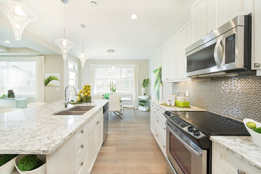 Offene, Zweizeilige Moderne Küche mit Unterbauwaschbecken, weißen Schränken, Rückwand aus Mosaikfliesen, Küchengeräten aus Edelstahl, hellem Holzboden und Kücheninsel in Calgary