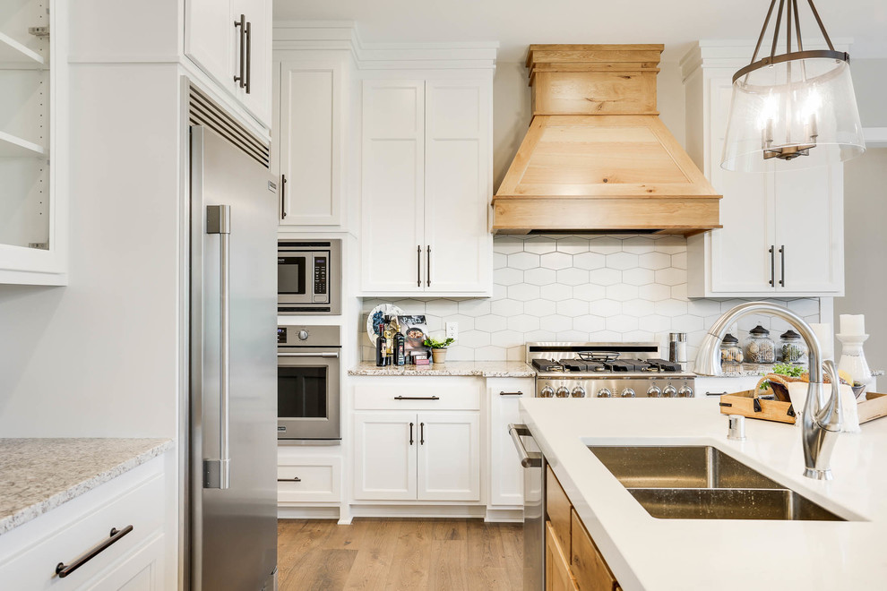 Design ideas for a traditional u-shaped kitchen in Minneapolis with a double-bowl sink, shaker cabinets, white cabinets, white splashback, stainless steel appliances, medium hardwood flooring, brown floors and white worktops.