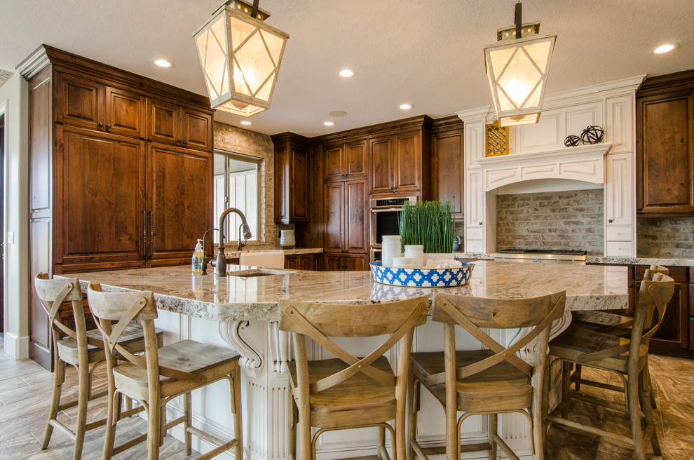 Eat-in kitchen - large craftsman galley ceramic tile eat-in kitchen idea in Salt Lake City with a farmhouse sink, raised-panel cabinets, medium tone wood cabinets, granite countertops, beige backsplash, stone tile backsplash, stainless steel appliances and an island