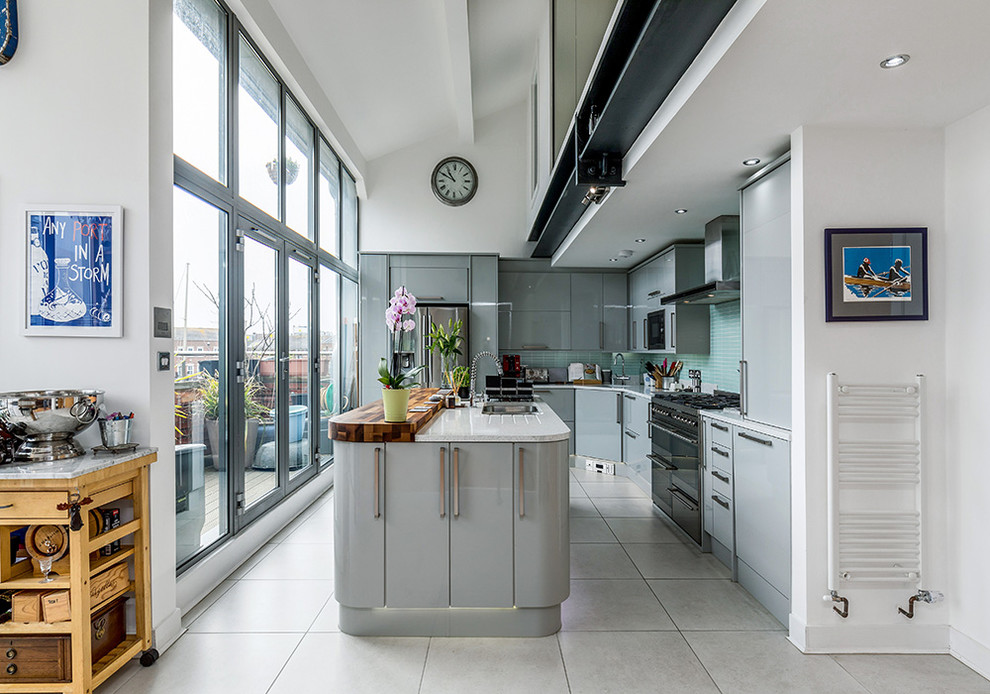 Foto på ett mellanstort funkis vit l-kök, med släta luckor, grå skåp, en köksö, grönt stänkskydd, svarta vitvaror, grått golv, en undermonterad diskho och stänkskydd i mosaik