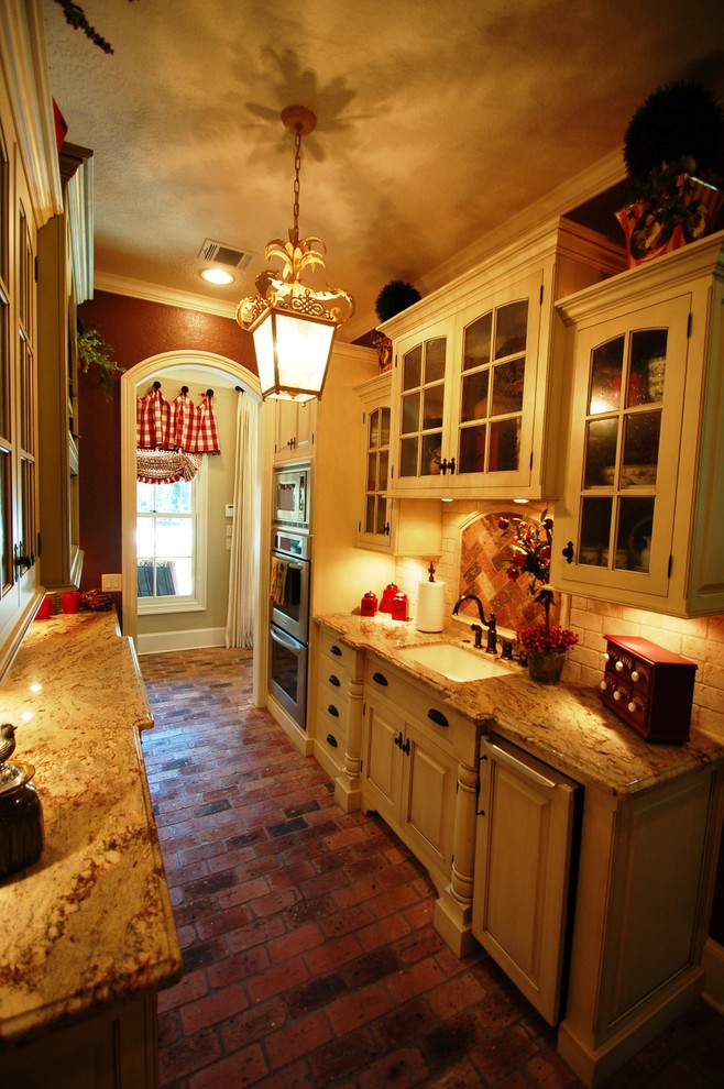 Foto på ett eklektiskt kök, med en nedsänkt diskho, luckor med profilerade fronter, vita skåp, granitbänkskiva, vitt stänkskydd, stänkskydd i tunnelbanekakel, integrerade vitvaror och tegelgolv
