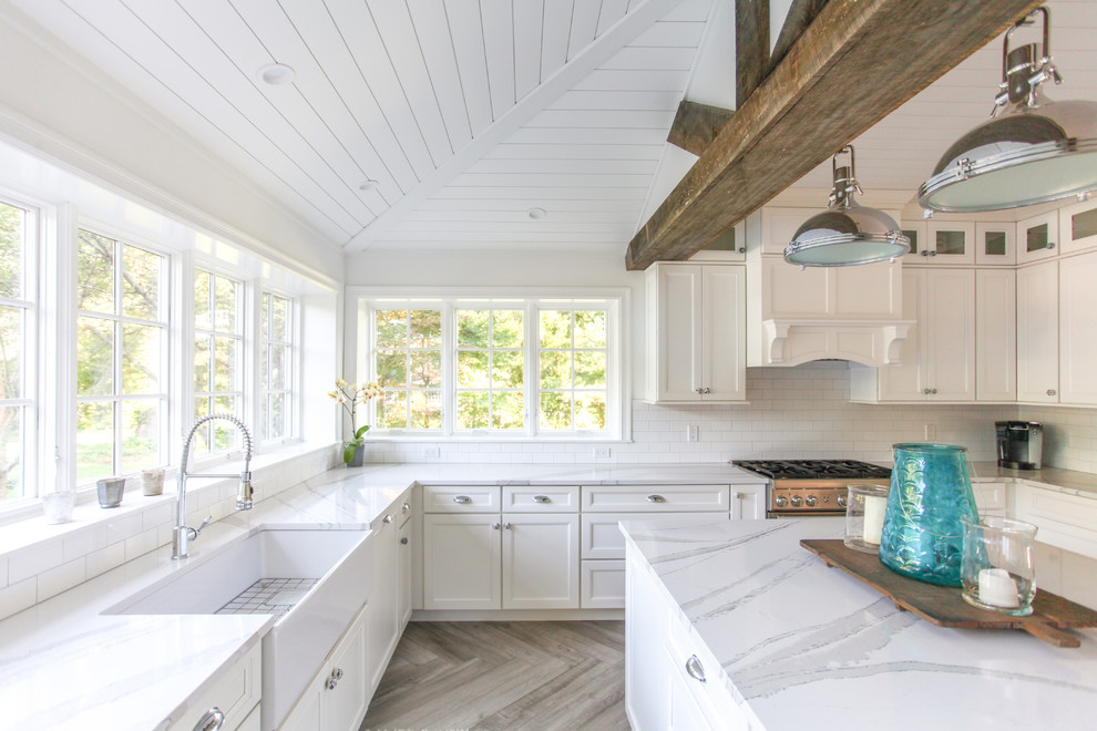 Inspiration for a large coastal u-shaped porcelain tile and gray floor eat-in kitchen remodel in New York with a farmhouse sink, shaker cabinets, white cabinets, quartz countertops, white backsplash, subway tile backsplash, paneled appliances, an island and white countertops