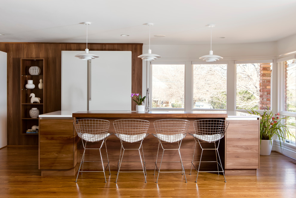 Modern inredning av ett stort kök med öppen planlösning, med en undermonterad diskho, släta luckor, vita skåp, rostfria vitvaror, mellanmörkt trägolv och en köksö